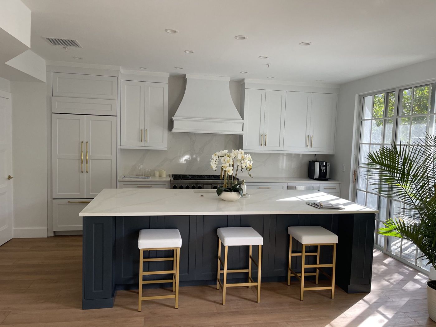 Remodeled kitchen with white cabinets, navy island and light wood floors